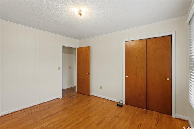 unfurnished bedroom featuring a textured ceiling, light hardwood / wood-style flooring, crown molding, and a closet