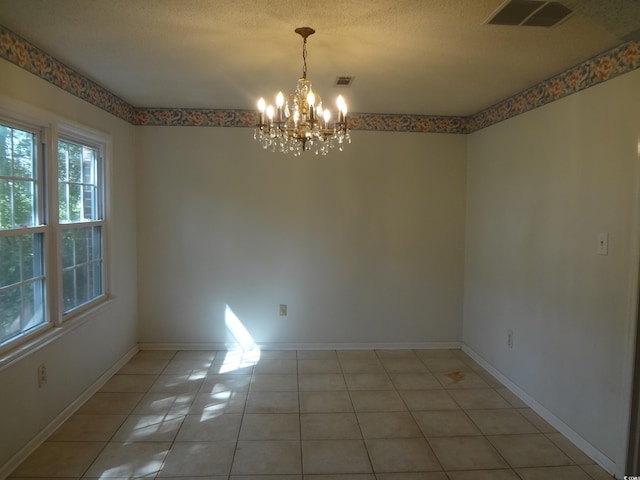 tiled empty room with a textured ceiling and a notable chandelier