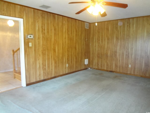 unfurnished room with light carpet, ceiling fan, and wood walls