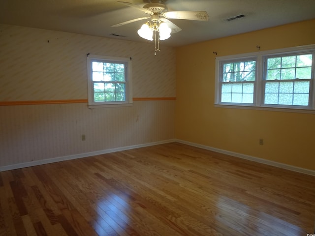 unfurnished room featuring wood-type flooring, a wealth of natural light, wooden walls, and ceiling fan