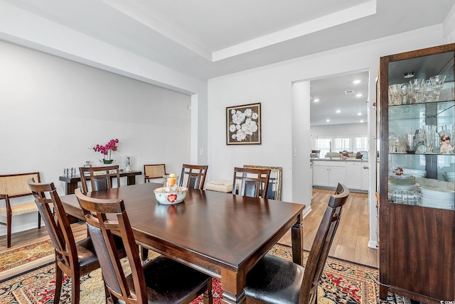 dining room with light hardwood / wood-style floors and a raised ceiling