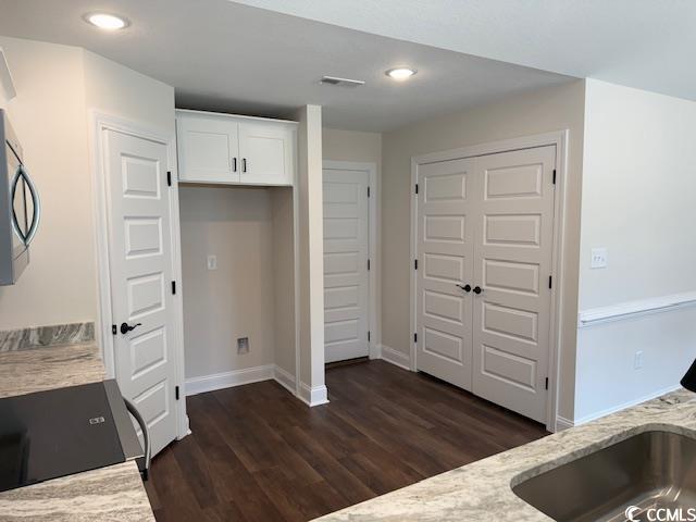 interior space featuring sink, dark wood-type flooring, light stone counters, stove, and white cabinets