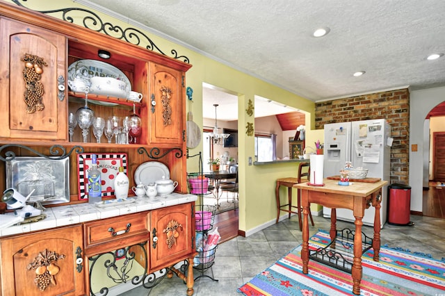 interior space featuring light tile patterned flooring, a textured ceiling, a chandelier, tile counters, and white refrigerator with ice dispenser