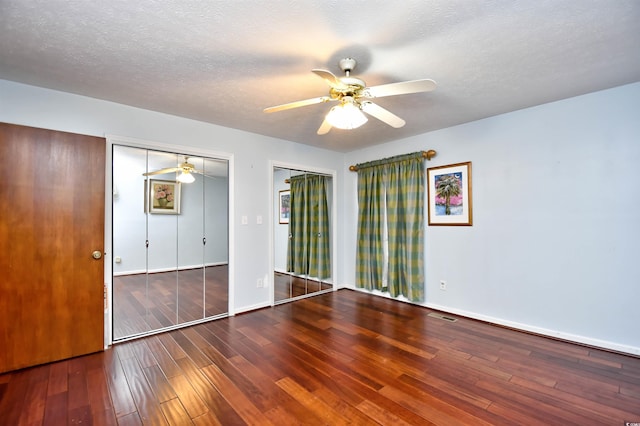 unfurnished bedroom featuring a textured ceiling, wood-type flooring, ceiling fan, and multiple closets