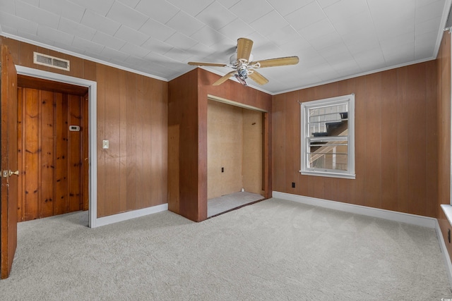 unfurnished bedroom featuring crown molding, wooden walls, light colored carpet, and ceiling fan