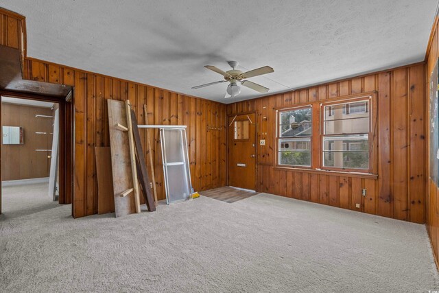 empty room with light carpet, wood walls, and a textured ceiling