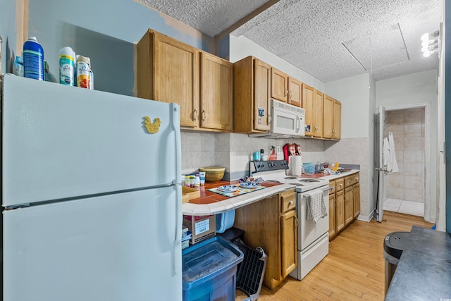 kitchen featuring tile walls, a textured ceiling, light wood-type flooring, and white appliances