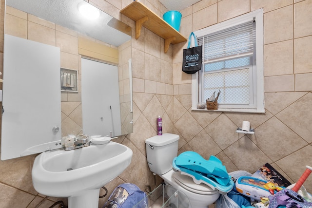 bathroom featuring tile walls, toilet, and a textured ceiling