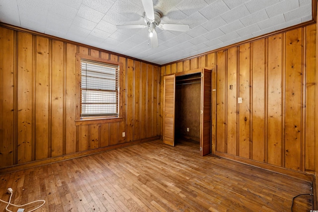 unfurnished bedroom featuring a closet, hardwood / wood-style floors, wooden walls, and ceiling fan