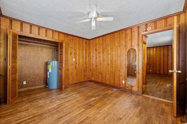 unfurnished bedroom featuring ceiling fan, wood walls, hardwood / wood-style flooring, a closet, and electric water heater