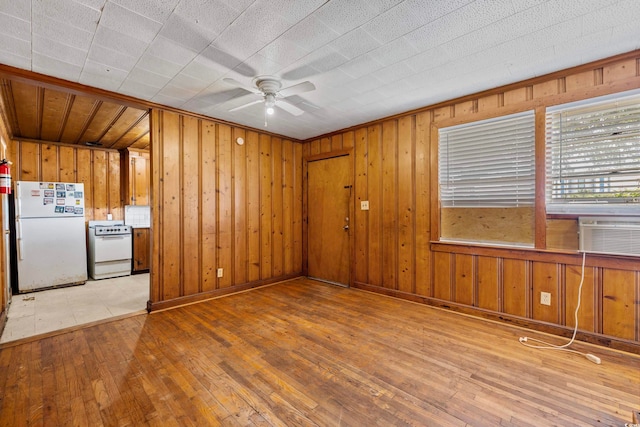 unfurnished living room featuring wooden walls, ceiling fan, cooling unit, and light hardwood / wood-style flooring