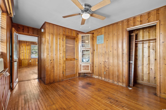 unfurnished bedroom with wood walls, a closet, hardwood / wood-style floors, and ceiling fan