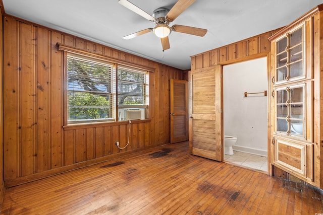 unfurnished bedroom featuring wooden walls, ceiling fan, hardwood / wood-style floors, ensuite bath, and cooling unit