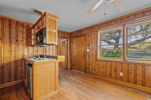 kitchen with white gas stovetop, wooden walls, light wood-type flooring, and ceiling fan