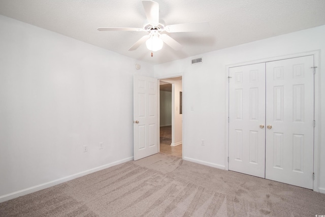 unfurnished bedroom featuring ceiling fan, a closet, light colored carpet, and a textured ceiling