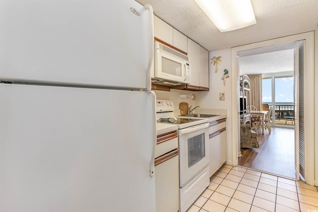 kitchen with light wood-type flooring, white appliances, floor to ceiling windows, white cabinets, and a textured ceiling