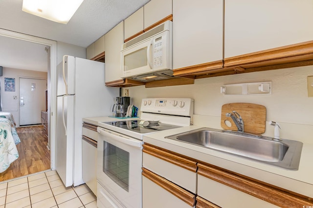 kitchen with sink, white appliances, a textured ceiling, white cabinetry, and light wood-type flooring