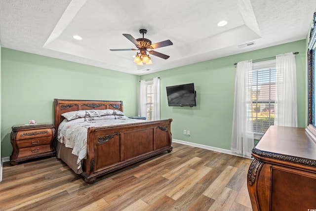 bedroom with ceiling fan, a raised ceiling, dark wood-type flooring, and multiple windows