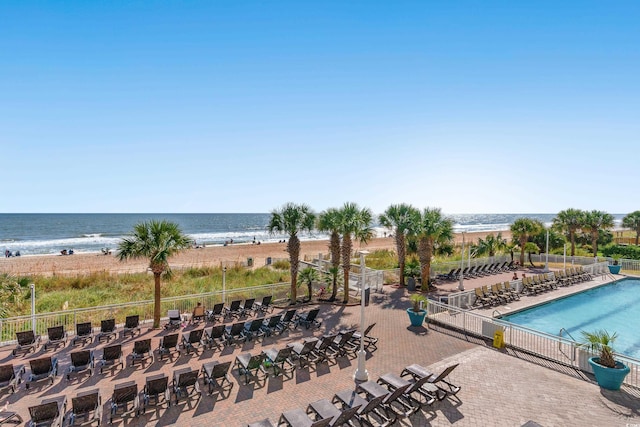 view of swimming pool with a water view, a view of the beach, and a patio area