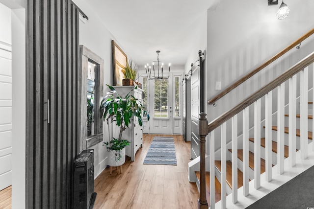 foyer with light hardwood / wood-style floors, an inviting chandelier, and a barn door