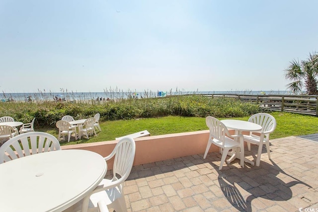 view of patio featuring fence, a beach view, outdoor dining space, and a water view
