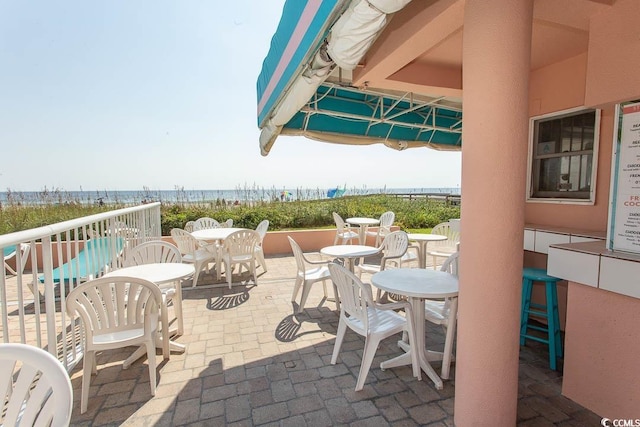 view of patio / terrace featuring a water view, a view of the beach, and outdoor dining space