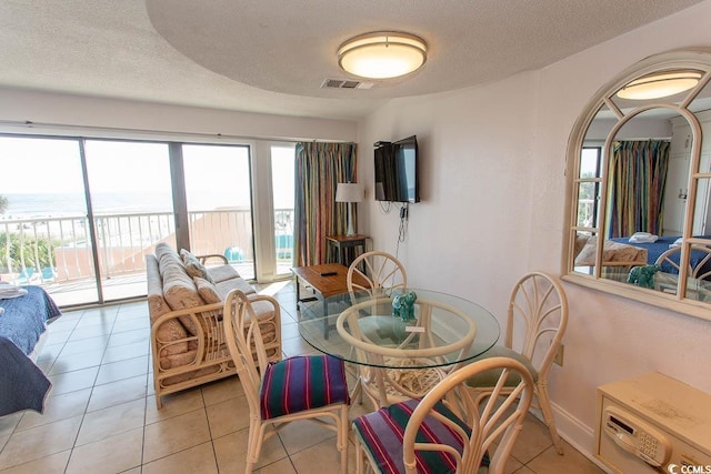 dining area with light tile patterned floors, a water view, a textured ceiling, and visible vents