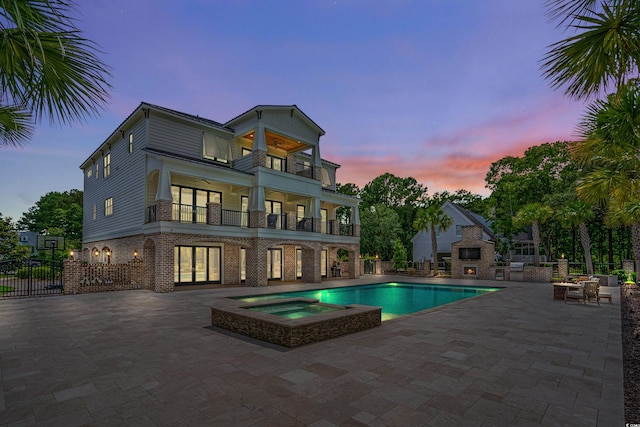 pool at dusk featuring an in ground hot tub and a patio