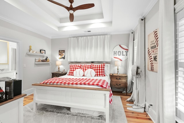 bedroom with light hardwood / wood-style floors, a tray ceiling, and ceiling fan