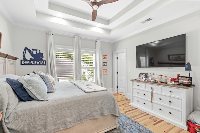 bedroom featuring ceiling fan, a raised ceiling, crown molding, and light hardwood / wood-style floors