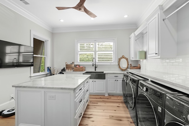 clothes washing area with ornamental molding, sink, light hardwood / wood-style flooring, cabinets, and washing machine and dryer