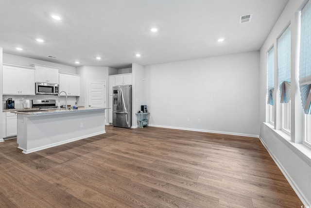 kitchen with dark wood-type flooring, appliances with stainless steel finishes, a kitchen island with sink, and white cabinets