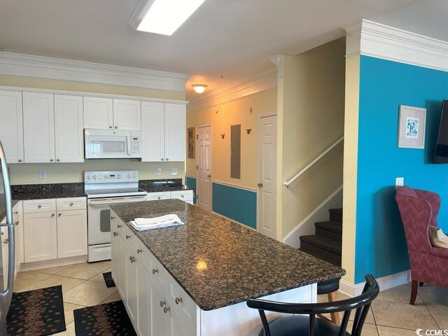 kitchen with ornamental molding, light tile patterned floors, white appliances, white cabinetry, and a center island