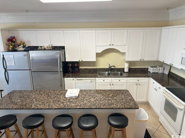 kitchen with white appliances, a breakfast bar, sink, ornamental molding, and white cabinetry