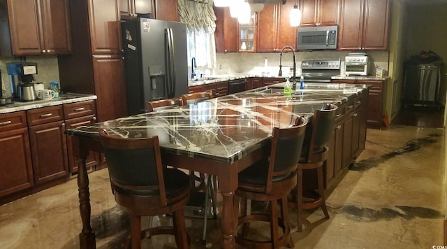 kitchen with a kitchen island with sink, stainless steel appliances, sink, and light stone countertops