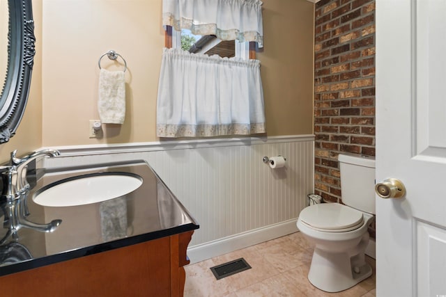 bathroom with toilet, vanity, tile patterned floors, and brick wall