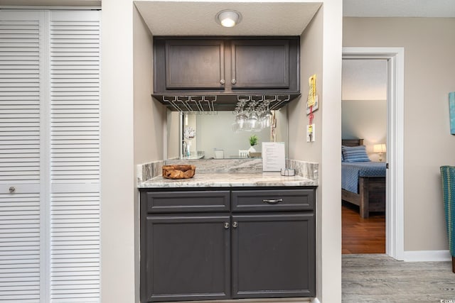 bar with dark brown cabinetry, light stone countertops, a textured ceiling, and light wood-type flooring