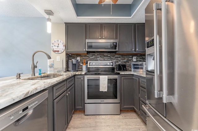 kitchen with stainless steel appliances, sink, pendant lighting, light hardwood / wood-style flooring, and a textured ceiling