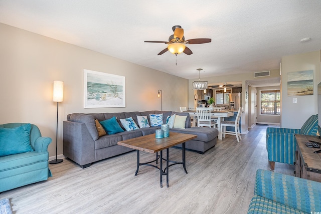 living room featuring light wood-type flooring, ceiling fan, and a textured ceiling