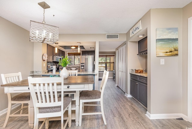 dining room featuring light wood-type flooring, an inviting chandelier, and a textured ceiling