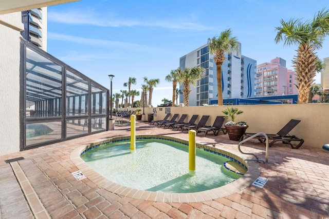 view of pool featuring glass enclosure, a patio, and a hot tub