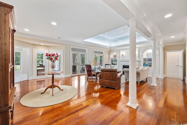 living area featuring wood-type flooring, crown molding, baseboards, and ornate columns