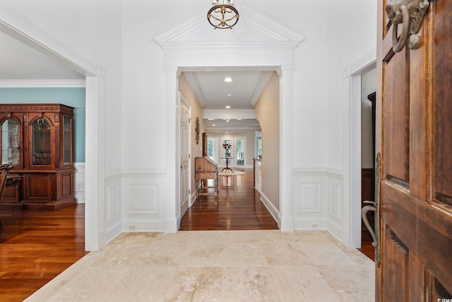 foyer entrance with crown molding, a wainscoted wall, and wood finished floors
