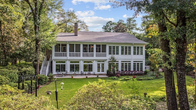 rear view of house with a lawn, a chimney, a patio, and a sunroom