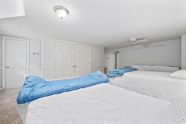 bedroom featuring carpet floors, a closet, visible vents, a ceiling fan, and a textured ceiling