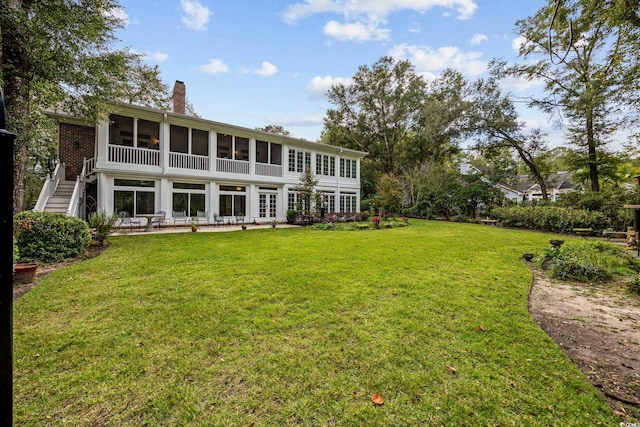 rear view of house featuring a sunroom, a yard, a patio area, and a chimney