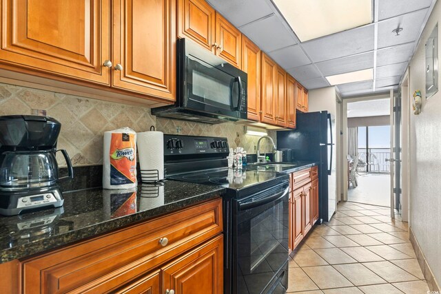 kitchen with black appliances, a drop ceiling, dark stone countertops, sink, and light tile patterned floors