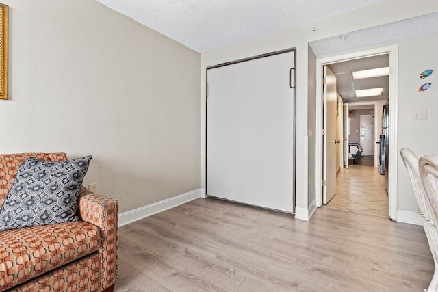 sitting room featuring light wood finished floors, baseboards, and a textured ceiling