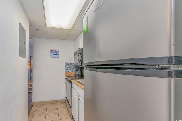 kitchen featuring a drop ceiling, light tile patterned floors, white cabinetry, and stainless steel appliances