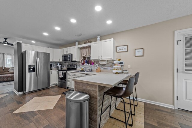 kitchen featuring white cabinetry, appliances with stainless steel finishes, dark wood-type flooring, and a breakfast bar area